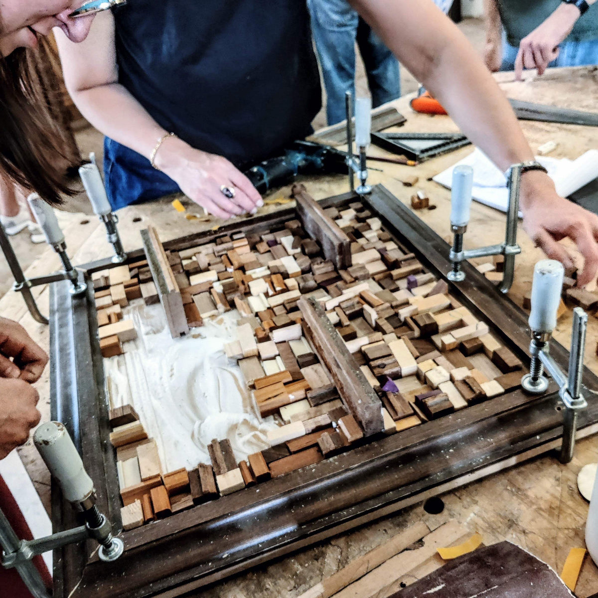 Een hout mozaïek in aanbouw van kleine stukjes hout. Met een bruine lijst en plankjes   om iets op te zetten. Gemaakt tijdens een Wall-Art teambuilding.
