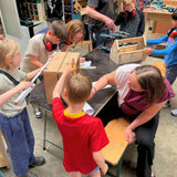 Kinderen zijn bezig met meten en tekenen hout tijdens een oudere en kind workshop.