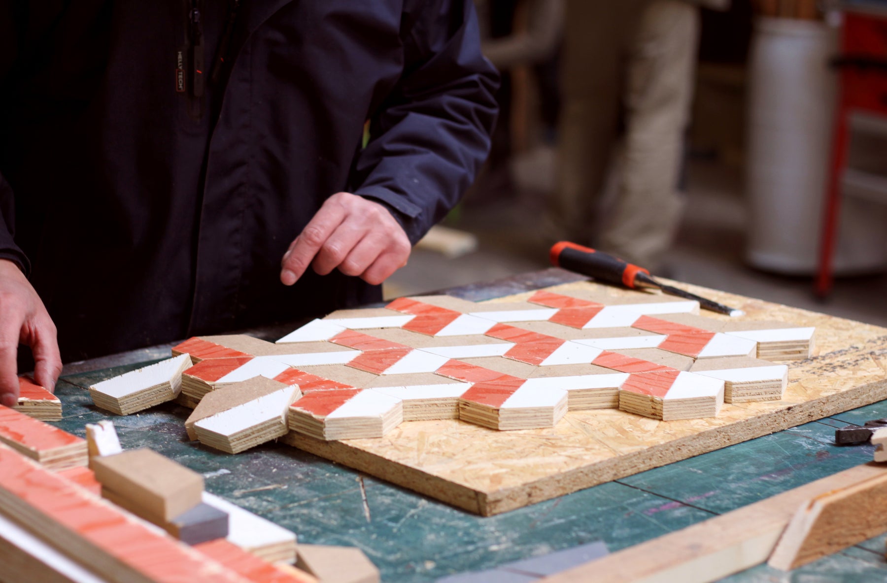 Er wordt een Hout mozaïek gelegd van verschillende trapezium vormige stukjes hout in rood, wit en bruin. Het wordt een decoratie voor aan de muur.