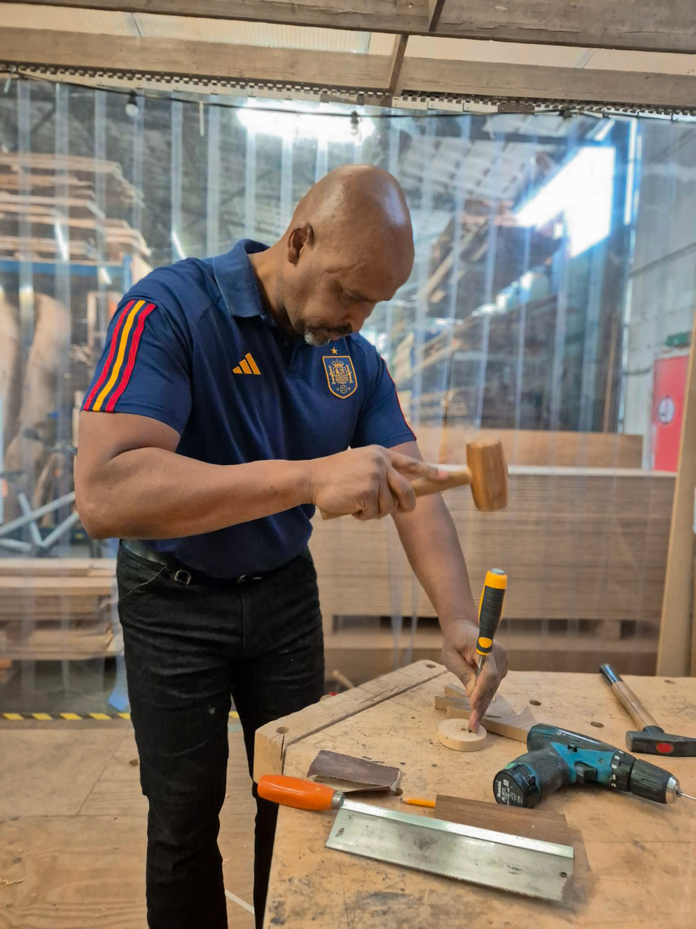 Een man is tijdens de workshop houten speelgoed maken, aan het werk met een beitel om een houten wiel aan te passen