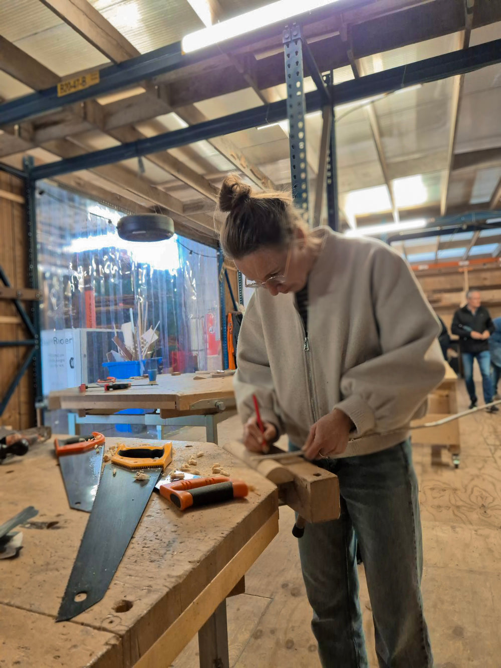 Een mevrouw is tijdens de workshop houten speelgoed maken, bezig met het aftekenen van een paal, om daar straks wielen van te zagen.