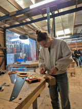 Een mevrouw is tijdens de workshop houten speelgoed maken, bezig met het aftekenen van een paal, om daar straks wielen van te zagen.