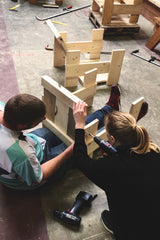 Twee deelnemers van de workshop Rietveld stoel samen aan het werk. Delen van de stoel worden aan elkaar geschroefd.